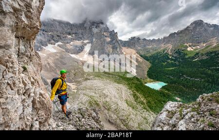 Young man, mountaineer on a fixed rope route, Via Ferrata Vandelli, view of Lago di Sorapis, Sorapiss circuit, mountains with low clouds, Dolomites Stock Photo