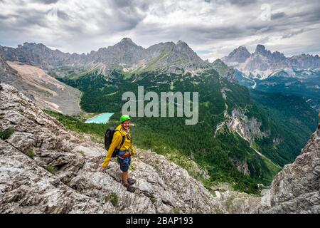 Young man, hiker on a fixed rope route, Via Ferrata Vandelli, view of Lago di Sorapis and the peaks of Cime de Laudo and Monte Cristallo, Sorapiss Stock Photo