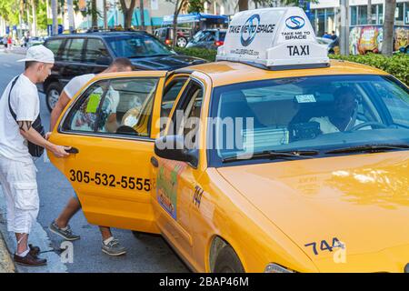 Miami Beach Florida,Washington Avenue,taxi,taxis,cab,cabs,transportation,man men male adult adults,enter,ride,vehicle,yellow,visitors travel traveling Stock Photo