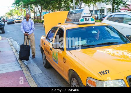 Miami Beach Florida,Washington Avenue,taxi,taxis,cab,cabs,Black man men male adult adults,passenger passengers rider riders,customer,luggage,suitcase, Stock Photo