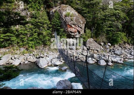 A tramper crosses a raging river using a narrow wire swing bridge Stock Photo