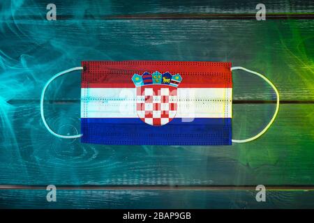 Medical mask for protection against airborne diseases, painted in the national flag of Croatia  on a black background in blue-green smoke. Medical pro Stock Photo