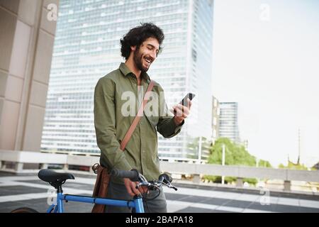 Handsome young man with beard and cycle using smartphone to read text message Stock Photo