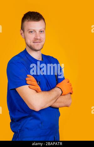 Young male worker in gloves and overalls. Male repair specialist. Professional for work. Yellow background Stock Photo