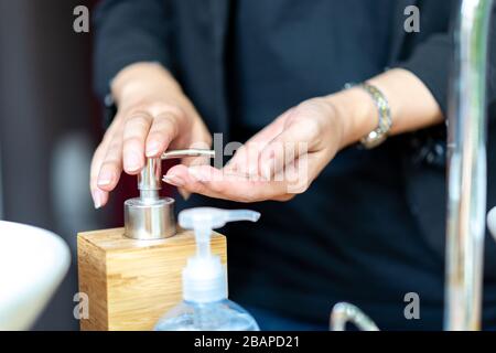 Business woman in dark black suit is puhsing washing soap on her hand beside the sink. Stock Photo