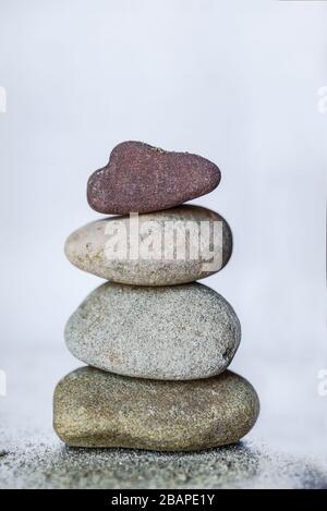 Four colored pebble Stones stacked on bright white background Stock Photo