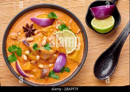A Chicken Massaman Curry in black bowl at dark slate background. Massaman Curry is Thai Cuisine dish with chicken meat, potato, onion and many spices. Stock Photo
