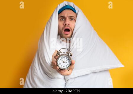 Emotional guy in blanket holding an alarm clock Stock Photo