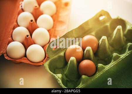 There are two packages of eggs on the white table. The red package contains white chicken eggs, and the green contains are three brown eggs. Stock Photo