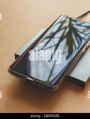 The phone is charging from a rectangular induction charger. Wireless charger Stock Photo