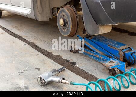 Car without wheel lifted with hydraulic floor jack and pneumatic impact wrench in a outdoors car workshop. Season tire changing procedure. Close view Stock Photo