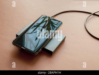 The phone is charging from a rectangular induction charger. Wireless charger. Copy space Stock Photo