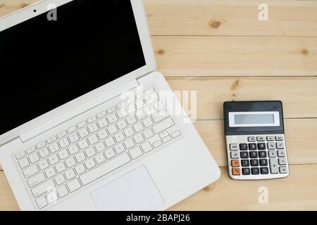 White laptop with calculator on wooden table, internet e-commerce concept. Stock Photo