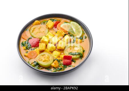 A Yellow Veg Thai Curry with Tofu and vegetables isolated on white background. Vegetarian Thai Curry with tofu, zucchini, bell pepper, spinach, carrot Stock Photo