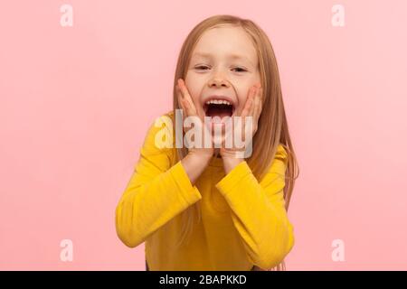 Happy surprised child emotions. Portrait of adorable little girl holding hands on face and screaming in amazement, keeping mouth wide open, shocked ex Stock Photo