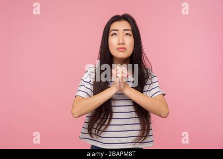 Please, I'm begging! Portrait of worried girl with long hair in t-shirt looking up and praying with imploring eyes, pleading for help, asking forgiven Stock Photo