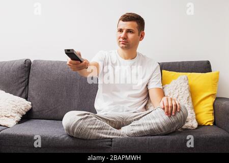 Young man sitting on sofa and holding tv remote control Stock Photo