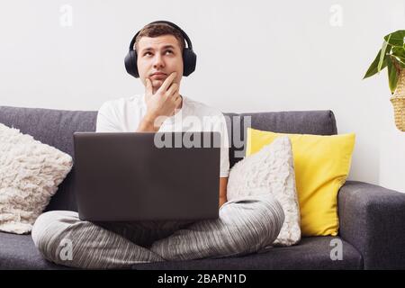 Doubtful young man looking up while working on laptop Stock Photo