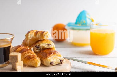 Breakfast with croissants, cinnamon buns and chocolate cookies, fresh orange juice and coffee on the side on a white background. Stock Photo