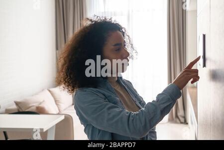African woman using smart home touch screen technology in apartment. Stock Photo