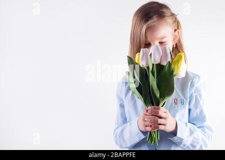Congratulation card with young beautiful girl holding bouquet of fresh tender tulips flowers in her hands against light grey background. Stock Photo