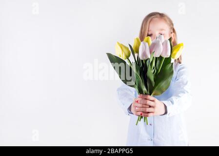 Congratulation card with young beautiful girl holding bouquet of fresh tender tulips flowers in her hands against light grey background. Stock Photo