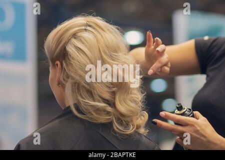 Closeup of hairdresser hands using hairspray styling on woman's healthy golden hair at barber salon Stock Photo