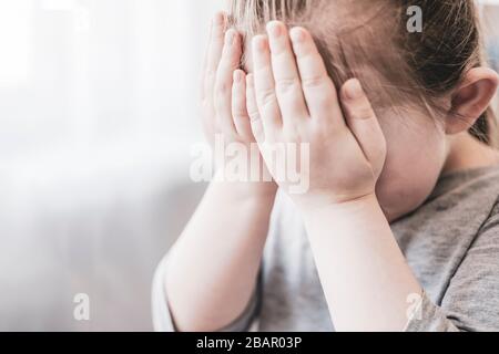 Little girl cries, covering her face with her hands. Stock Photo