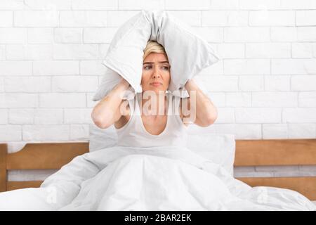 Mature lady in bed covering head with pillow Stock Photo