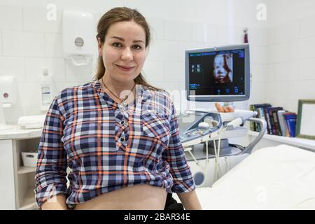 Portrait of pregnant woman in a hospital room with 3d model of fetus on screen of ultrasonography apparatus Stock Photo