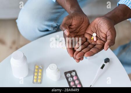 Coronavirus therapy. Closeup of African american man holding drugs indoors, top view. Empty space Stock Photo