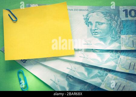 Brazilian money, 100 reais banknotes on green background with blank yellow card for text Stock Photo