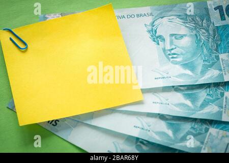 Brazilian money, 100 reais banknotes on green background with blank yellow card for text Stock Photo