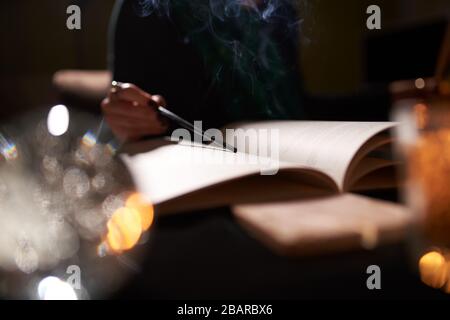 Fortune teller with open book of predictions on table with candles, close-up Stock Photo