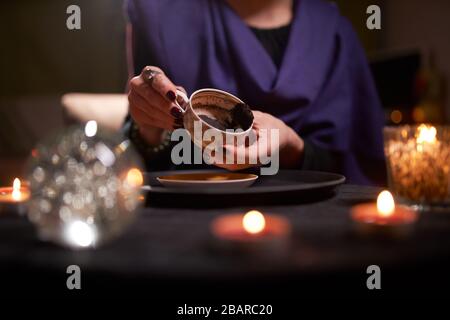 Close-up of woman fortuneteller's hands divining on coffee grounds at table with predictive ball in room Stock Photo