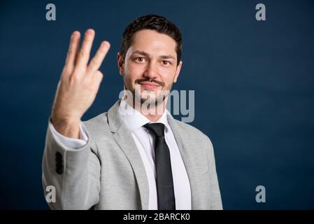 Portrait of business young handsome male showing number three gesture on blue background with copy space advertising area Stock Photo