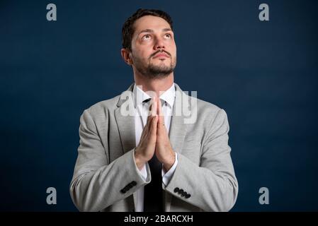 Portrait of business young handsome male making prayer gesture on blue background Stock Photo