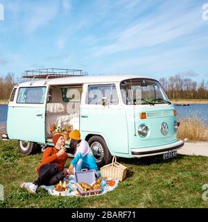 Noordoostpolder Netherlands April 2019, Classic Green and white VW Camper Van parked with couple watching the Sunrise over the meadow during Spring Stock Photo