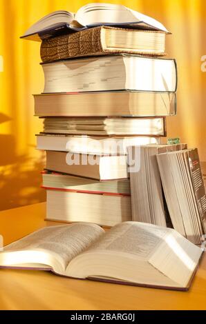 A pile of books on he fair wooden table agaist vibrant yellow wal with shadows Stock Photo