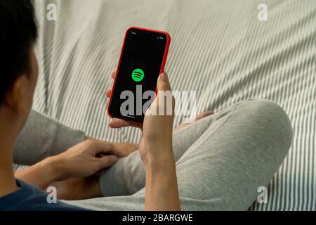 BANGKOK,THAILAND - MARCH 27, 2020: A man holding a phone with screenshot of Spotify on iPhone. Spotify is an international media services provider Stock Photo