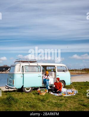 Noordoostpolder Netherlands April 2019, Classic Green and white VW Camper Van parked with couple watching the Sunrise over the meadow during Spring Stock Photo