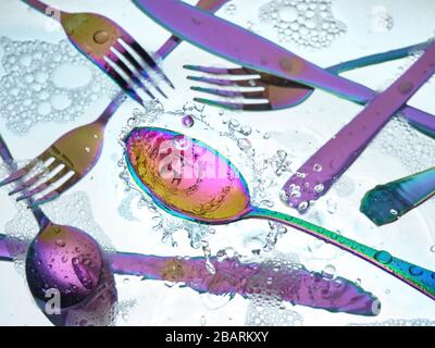 Washing colorful silverware in kitchen sink with splashes and bubbles Stock Photo