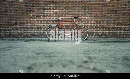 Retro styled red Singlespeed fixed gear bike leaning isolated on a brick wall Stock Photo