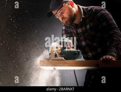 Construction worker crosses a board with a circular saw. Stock Photo