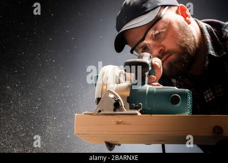 Construction worker crosses a board with a circular saw. Stock Photo