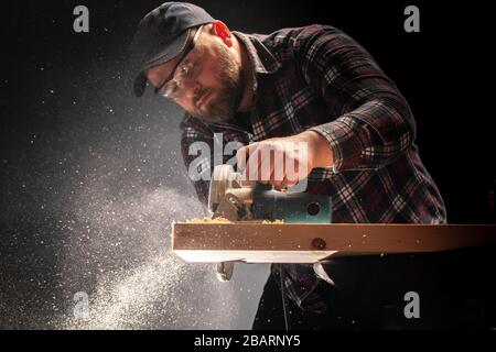 Construction worker crosses a board with a circular saw. Stock Photo
