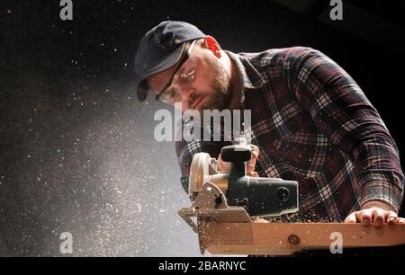 Construction worker crosses a board with a circular saw. Stock Photo