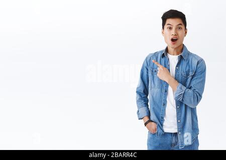 Portrait of excited and impressed asian man hearing awesome event going nearby, look camera astonished open mouth talking about product on the left Stock Photo