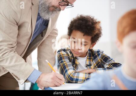 Portrait of cute African-American boy listening to teacher while sitting at desk in school classroom Stock Photo