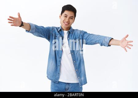 Portrait of friendly charismatic young handsome taiwanese man reaching you for tight warm hug, stretch hands sideways smiling, invite give warm Stock Photo